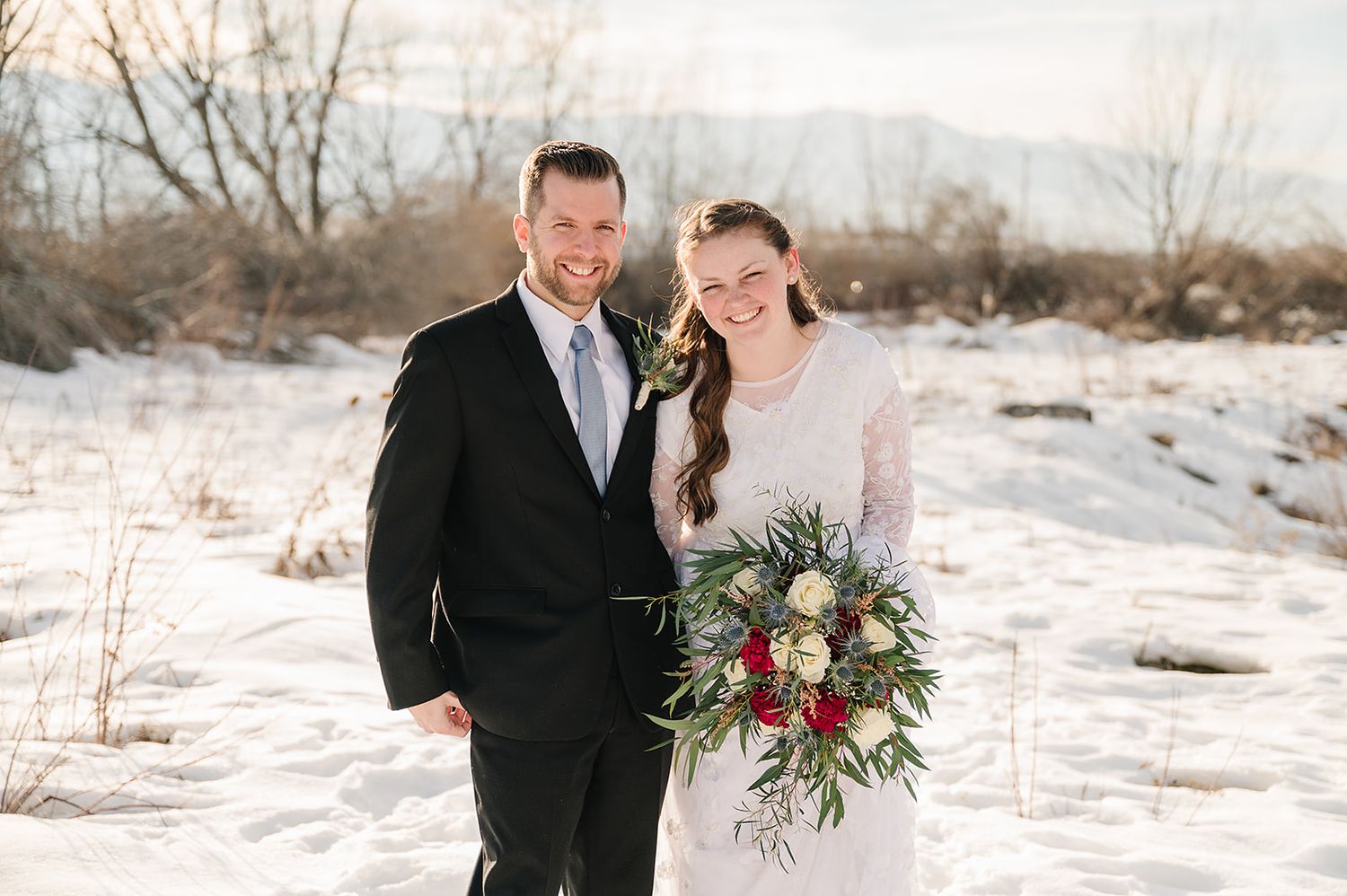 A winter wedding portrait with snow-covered ground and bare trees in the background.
