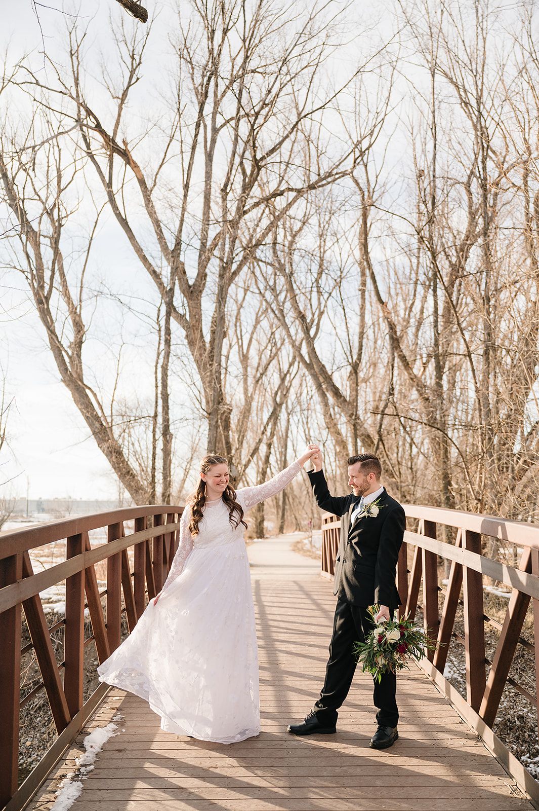 A couple dancing on a wooden bridge surrounded by winter trees.
