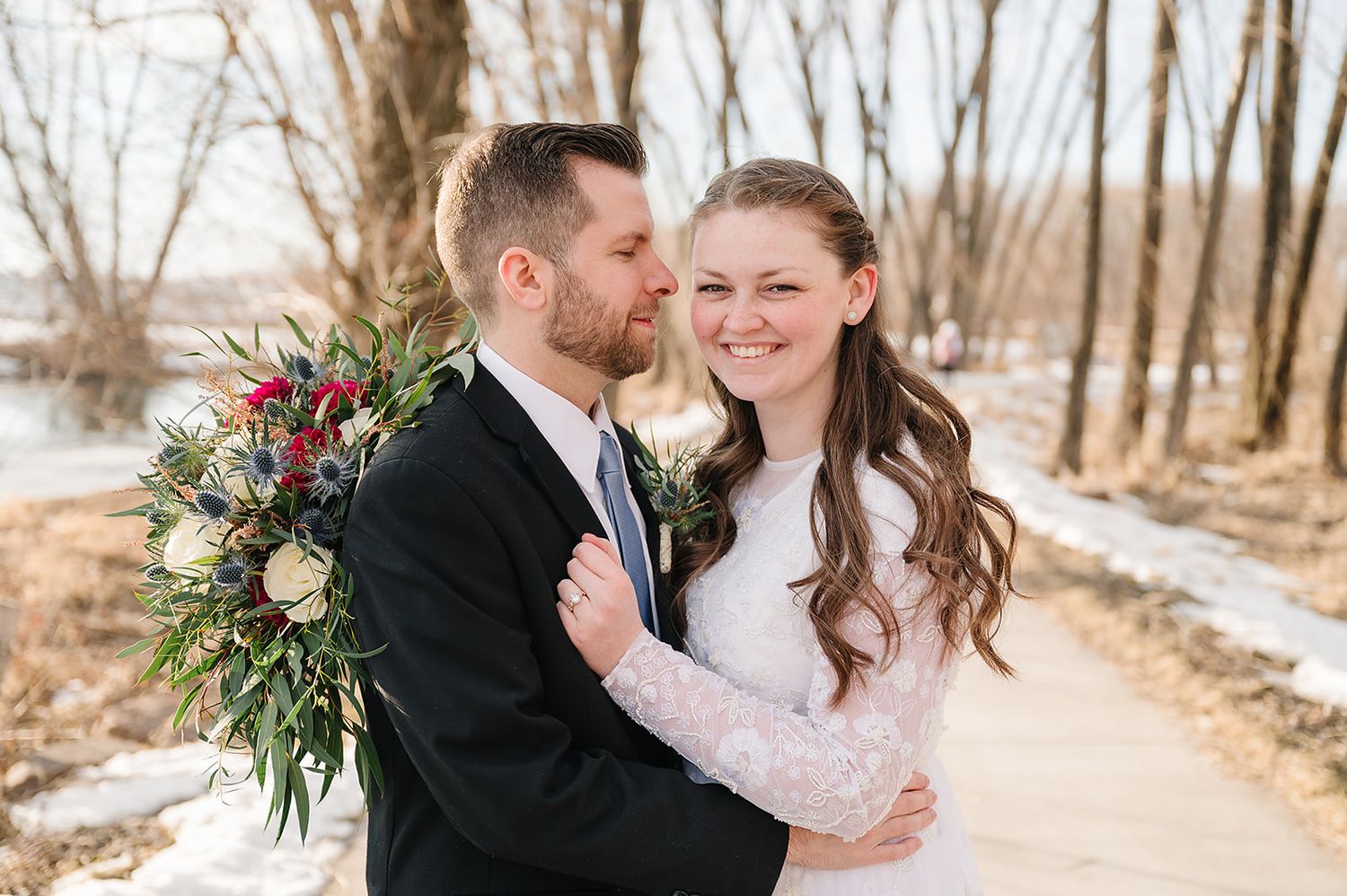 A romantic winter wedding portrait on a snowy path with natural foliage.