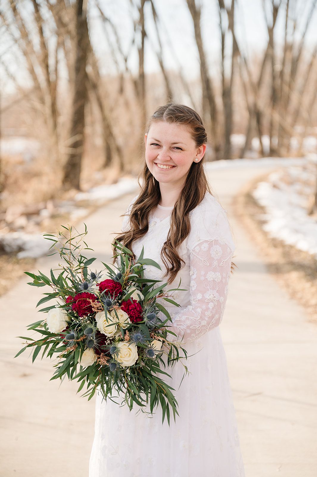 A winter wedding portrait with a bride holding a burgundy and white floral bouquet.