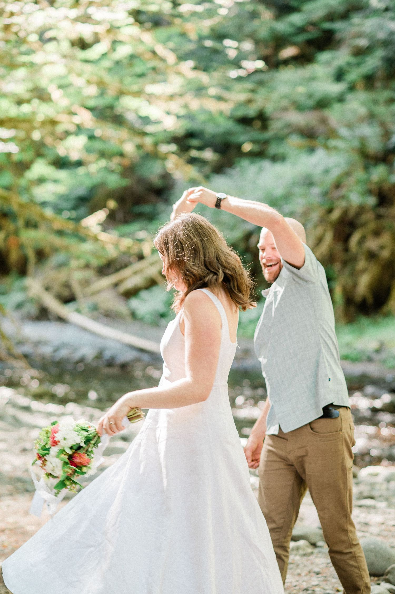 A couple in wedding attire dances joyfully together in a lush forest setting during Olympic National Park elopement
