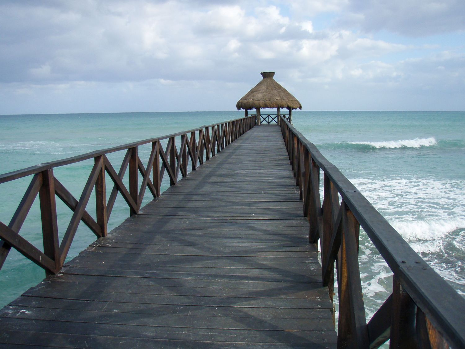 A wooden pier with thatched roof gazebo extends into turquoise Caribbean waters.