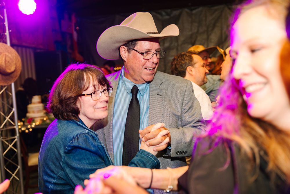 Guests dance and celebrate at a western-themed wedding reception under colored lights.