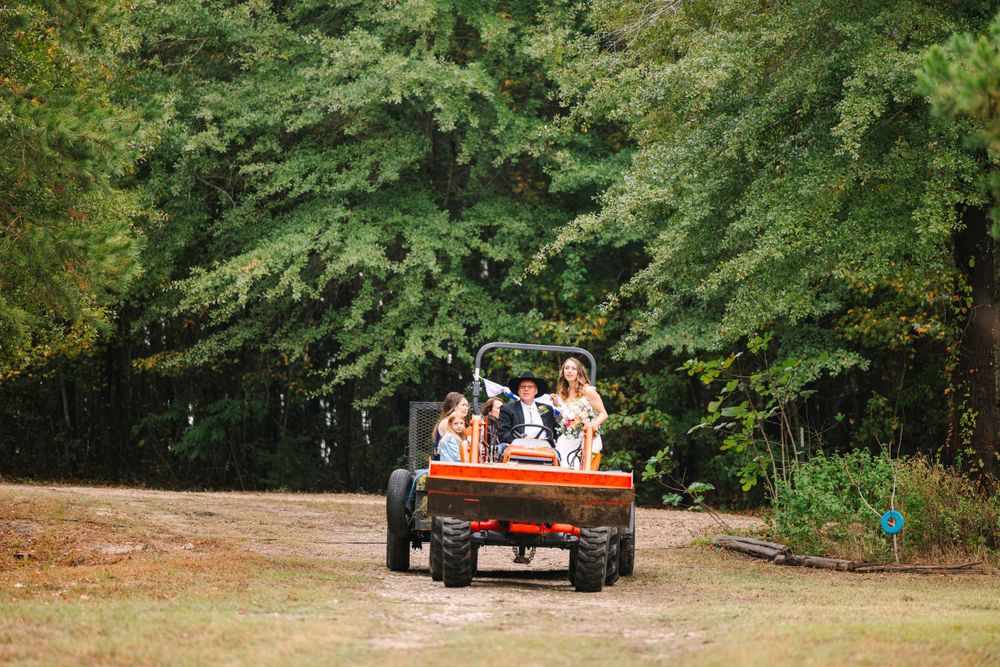 Wedding party riding in the back of a red utility vehicle through a wooded area.
