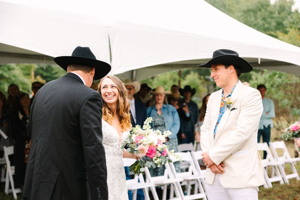 Outdoor wedding ceremony under a white tent with casual western-themed attire.