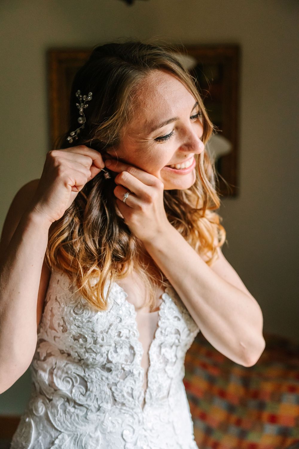 A bride putting on earrings while getting ready in a naturally lit room.
