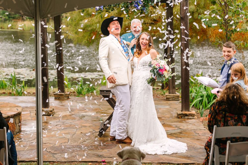 Wedding couple celebrates during ceremony under pergola with confetti and autumn foliage.