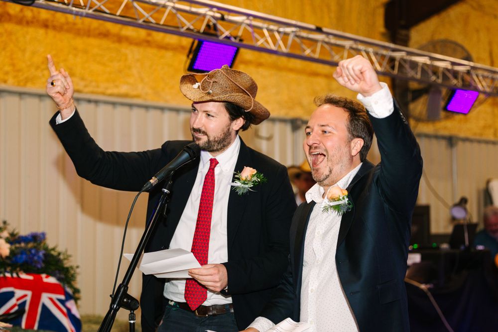 Two people celebrating enthusiastically on stage with arms raised at an event with overhead lighting.