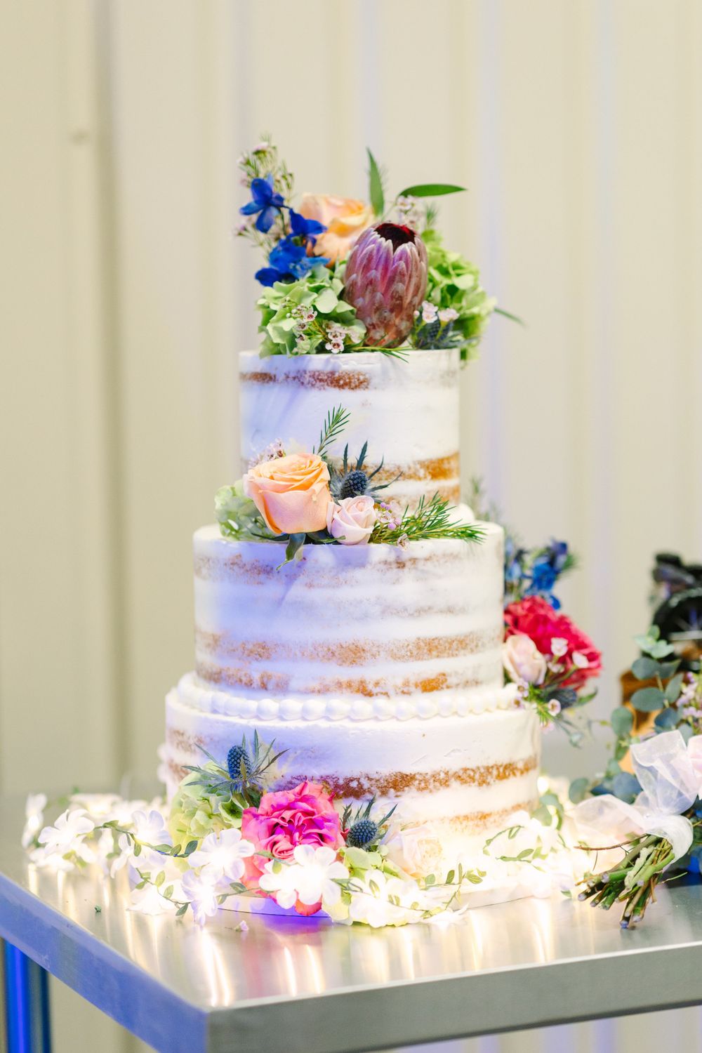 Four-tier semi-naked wedding cake decorated with fresh flowers and fairy lights.