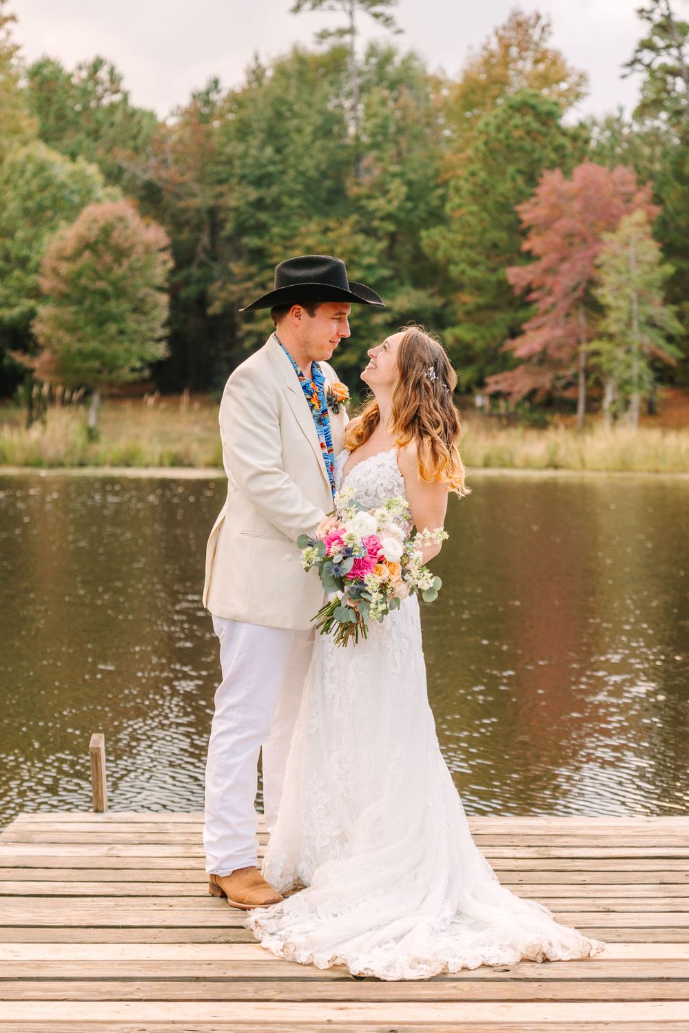 Couple shares intimate moment on wooden dock overlooking serene lake during autumn wedding.