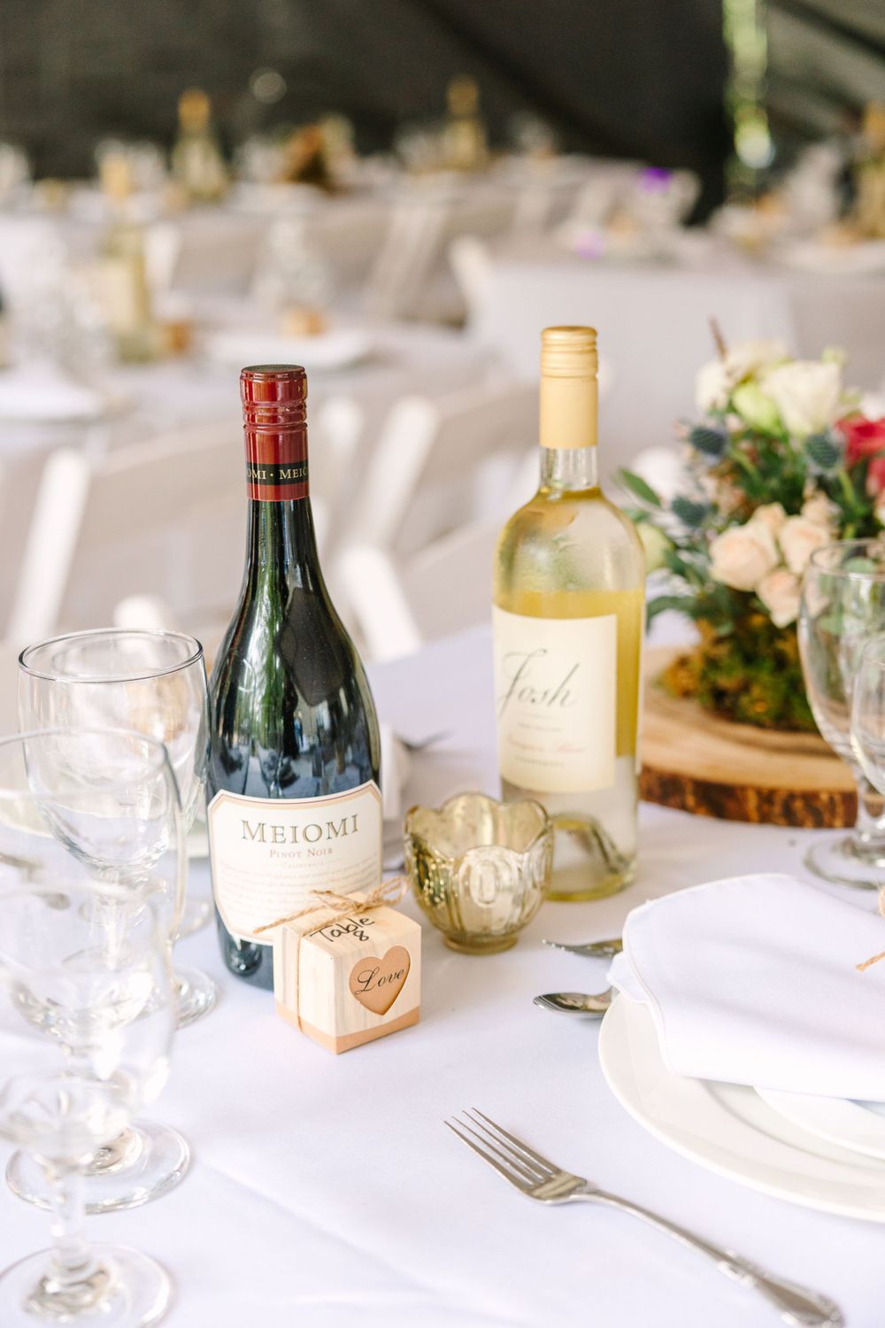 Wedding table setting with wine bottles, glasses, and floral centerpiece on white tablecloth.
