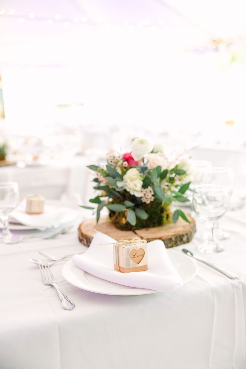 Elegant wedding table setting with floral centerpiece on wood slice and custom place card.