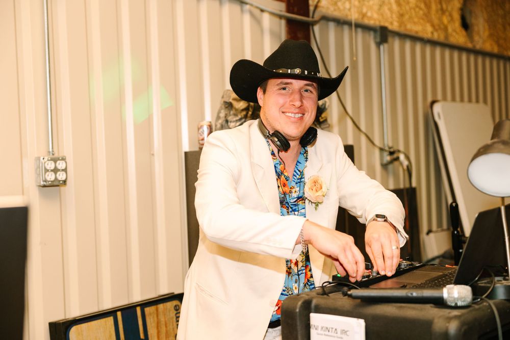 DJ in cowboy hat and white blazer working the sound equipment at an event.