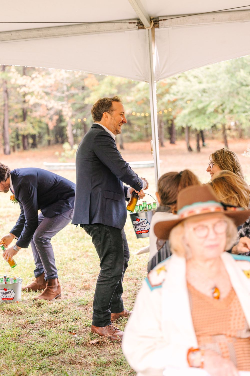 Wedding guests enjoying festivities under a white tent during an outdoor celebration.