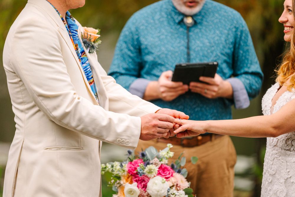 Close up of couple exchanging rings during outdoor wedding ceremony.