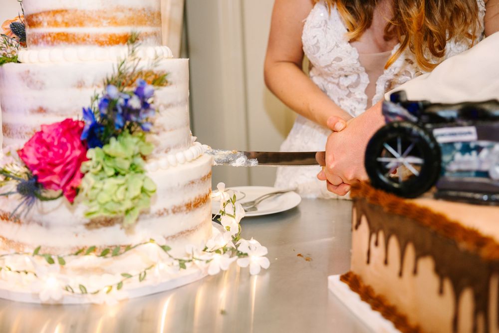 Close-up of a tiered wedding cake with pink and blue florals and chocolate drip details.