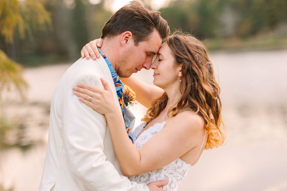 Romantic close-up of couple sharing intimate moment in white wedding attire by lake.