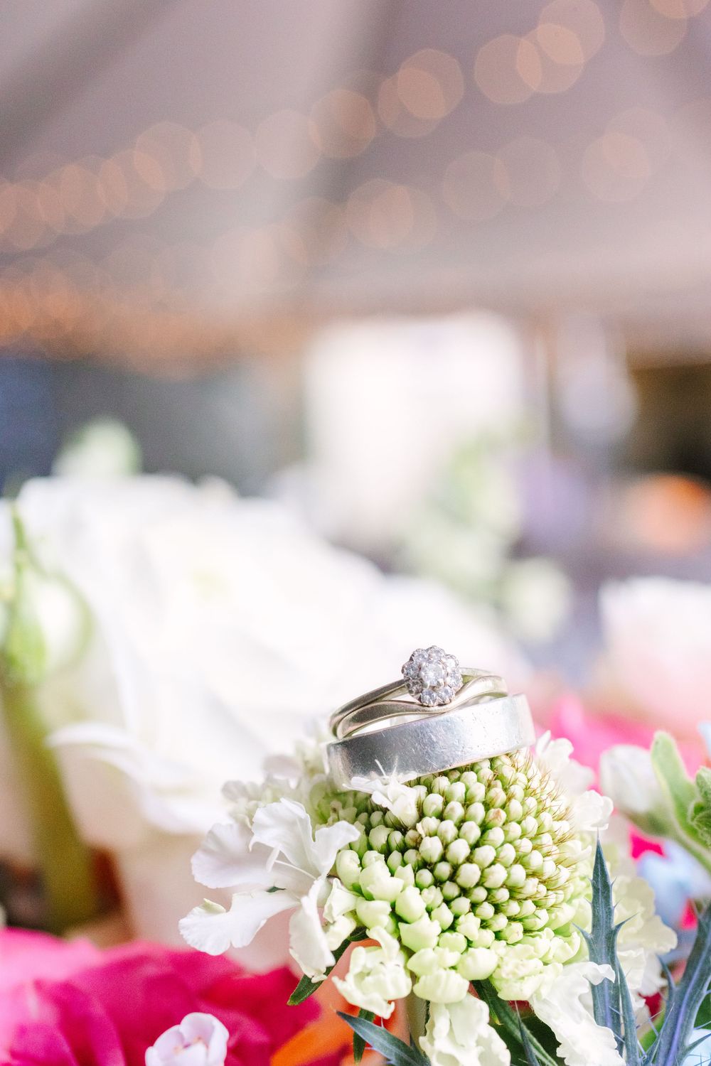 Wedding ring photographed on a white flower with soft bokeh lights in the background.