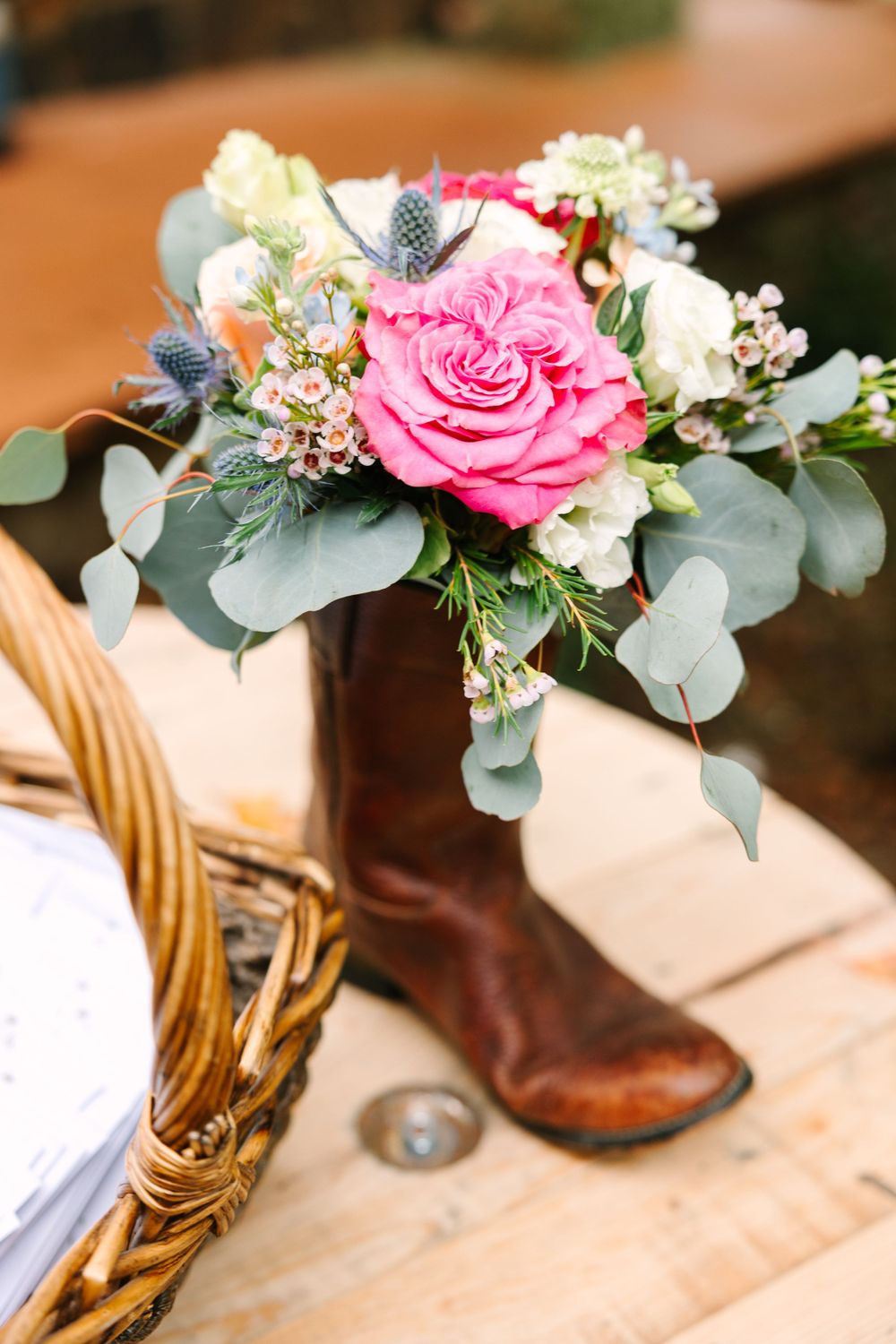 Pink rose and eucalyptus floral arrangement displayed in a rustic brown boot.