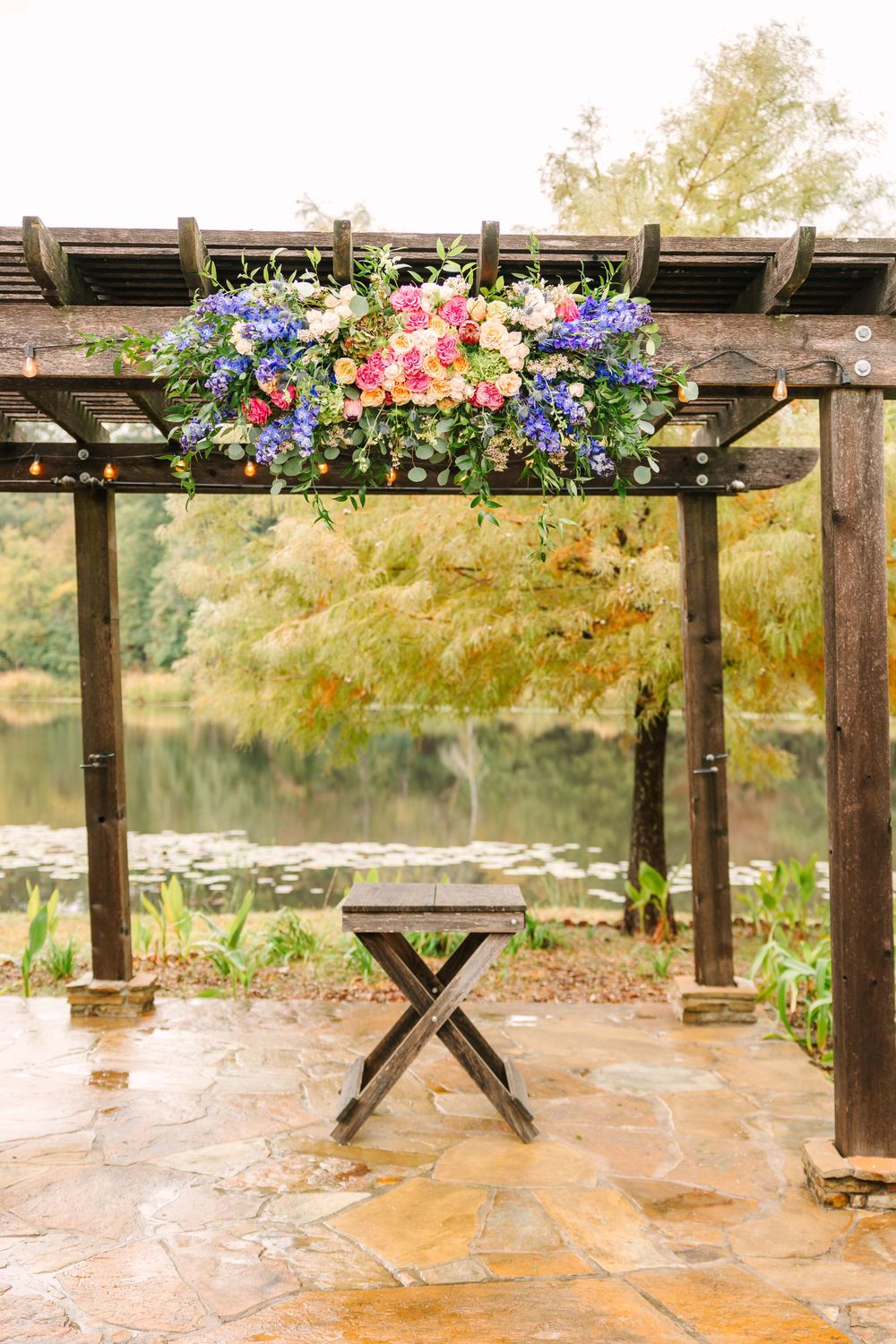 Wooden pergola with colorful floral arrangements of pink and blue flowers over stone patio.