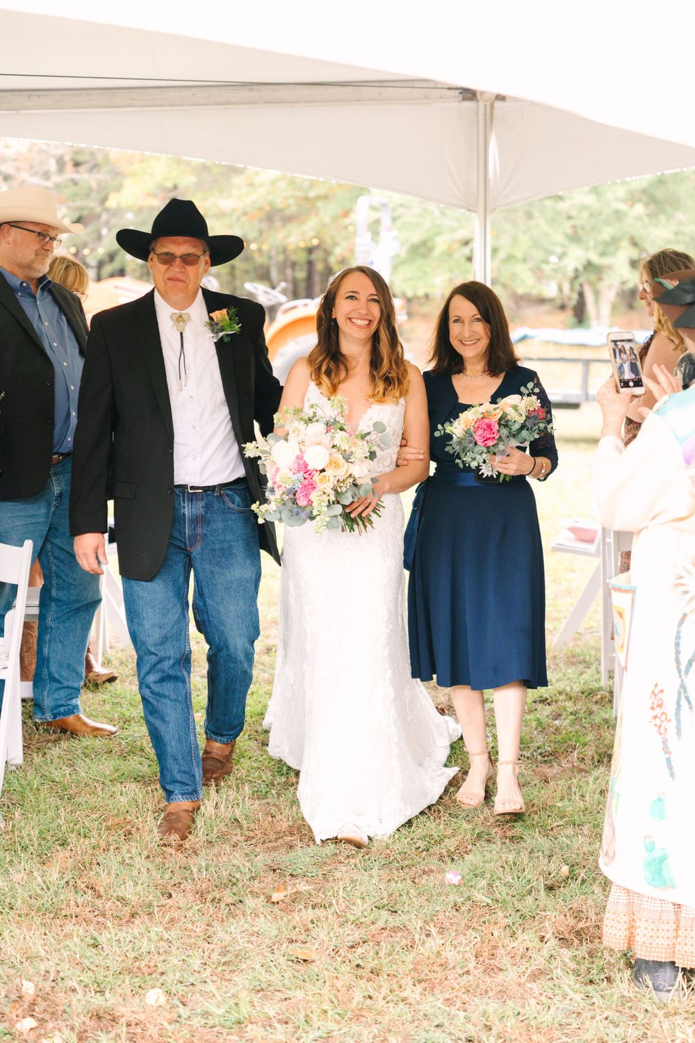 Wedding party in casual western attire walking under a white tent during an outdoor celebration.