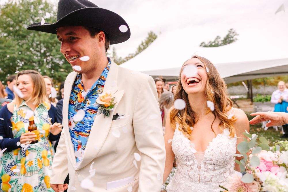 Joyful couple laughs during outdoor wedding celebration with guests.
