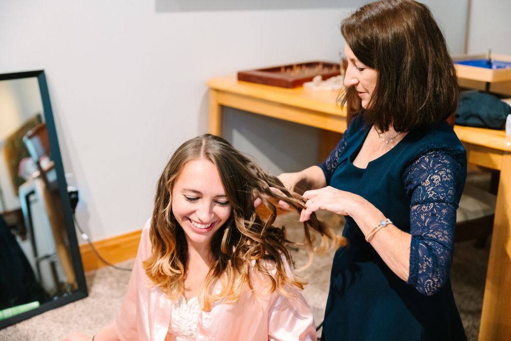 Hair stylist working on bride's hairstyle in preparation room.