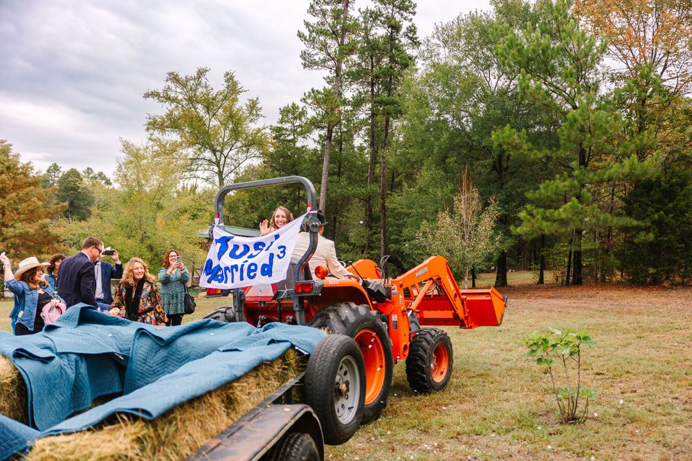 Wedding celebration with decorated tractor and hay bales in rustic outdoor setting.