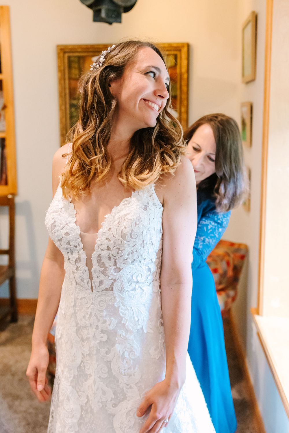 A bride in a detailed lace wedding dress smiling during wedding preparations.