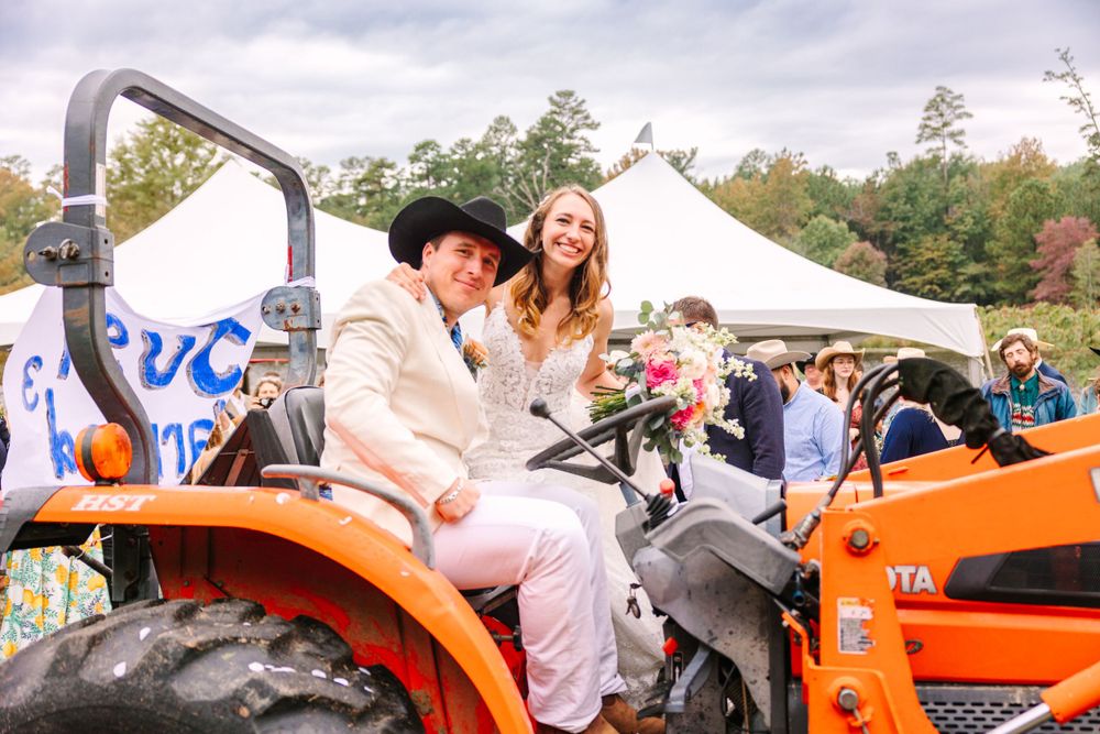 Newlyweds sitting together on orange tractor at country wedding reception.