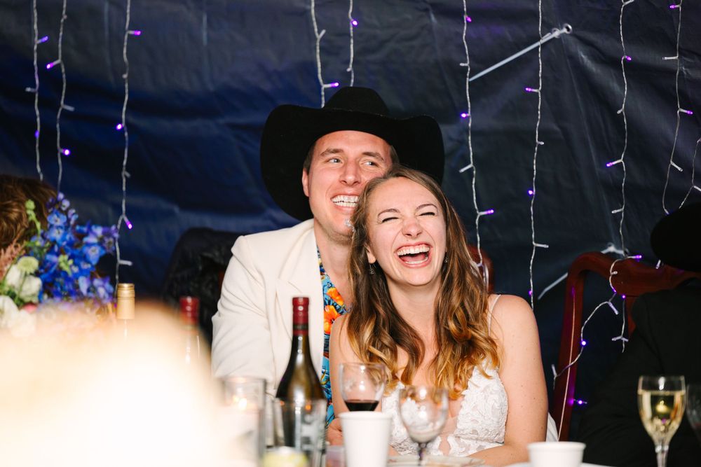 Party guests share a joyful moment at a wedding reception with string lights and blue decorations.