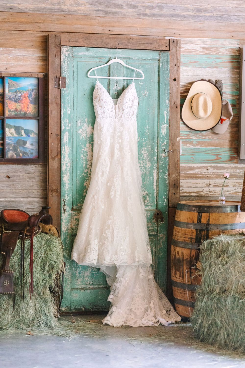 Elegant lace wedding dress hanging on vintage mint green door with straw bales and rustic decor.