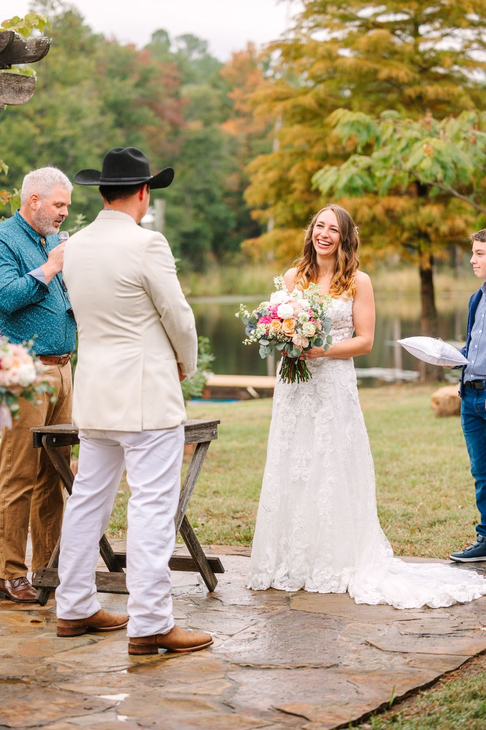 Wedding ceremony in autumn with a person in white suit and lace wedding dress holding bouquet.