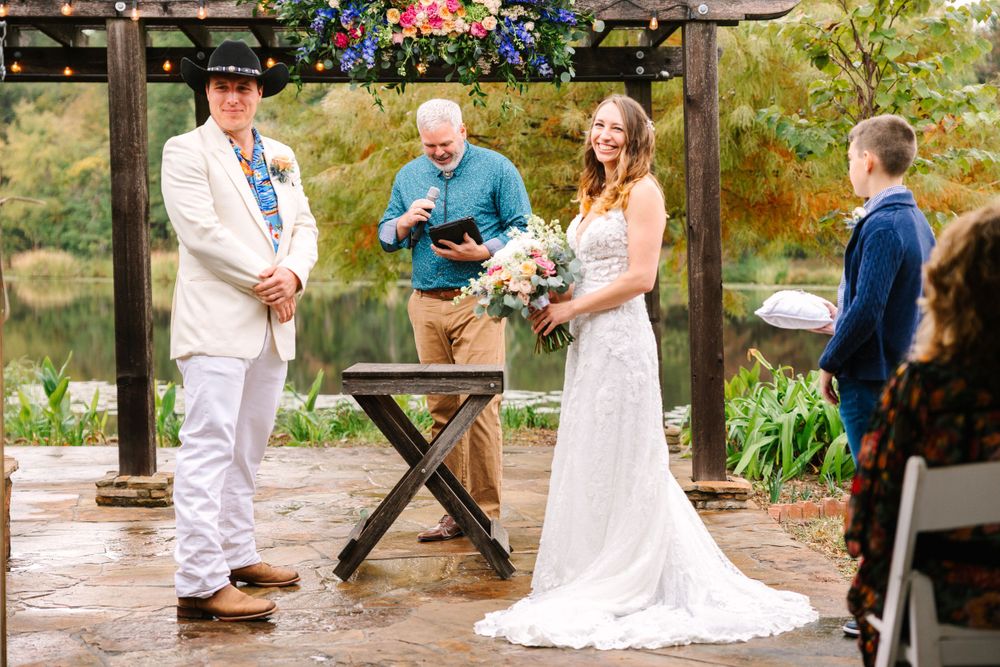 Wedding ceremony taking place under a wooden pergola with floral decorations.