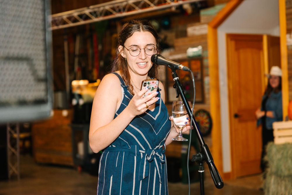 Someone in a striped dress speaks into a microphone at an indoor venue.
