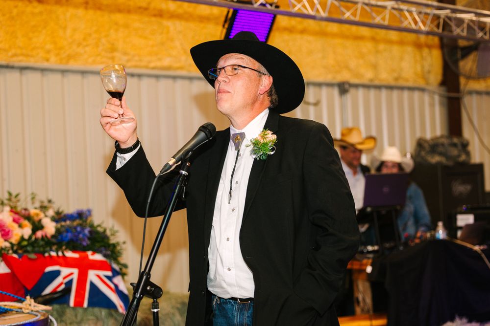 A person in formal wear and cowboy hat makes a toast speech at a reception with stage lighting.