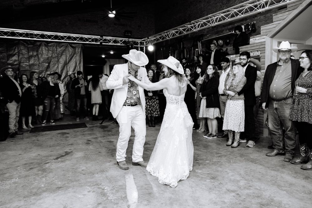 A black and white image shows a couple performing a dance move at their wedding celebration.