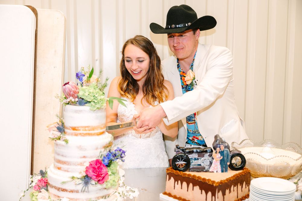 A couple cuts their wedding cake decorated with pink and blue flowers and a black drip design.