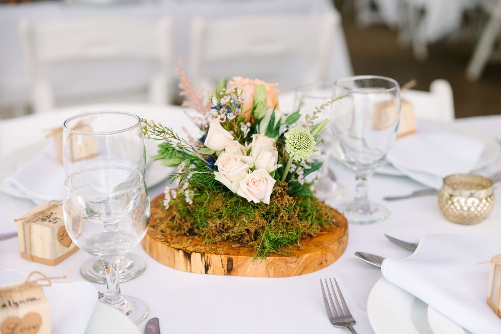 Rustic wedding centerpiece with fresh flowers on wood slice charger and white table setting.
