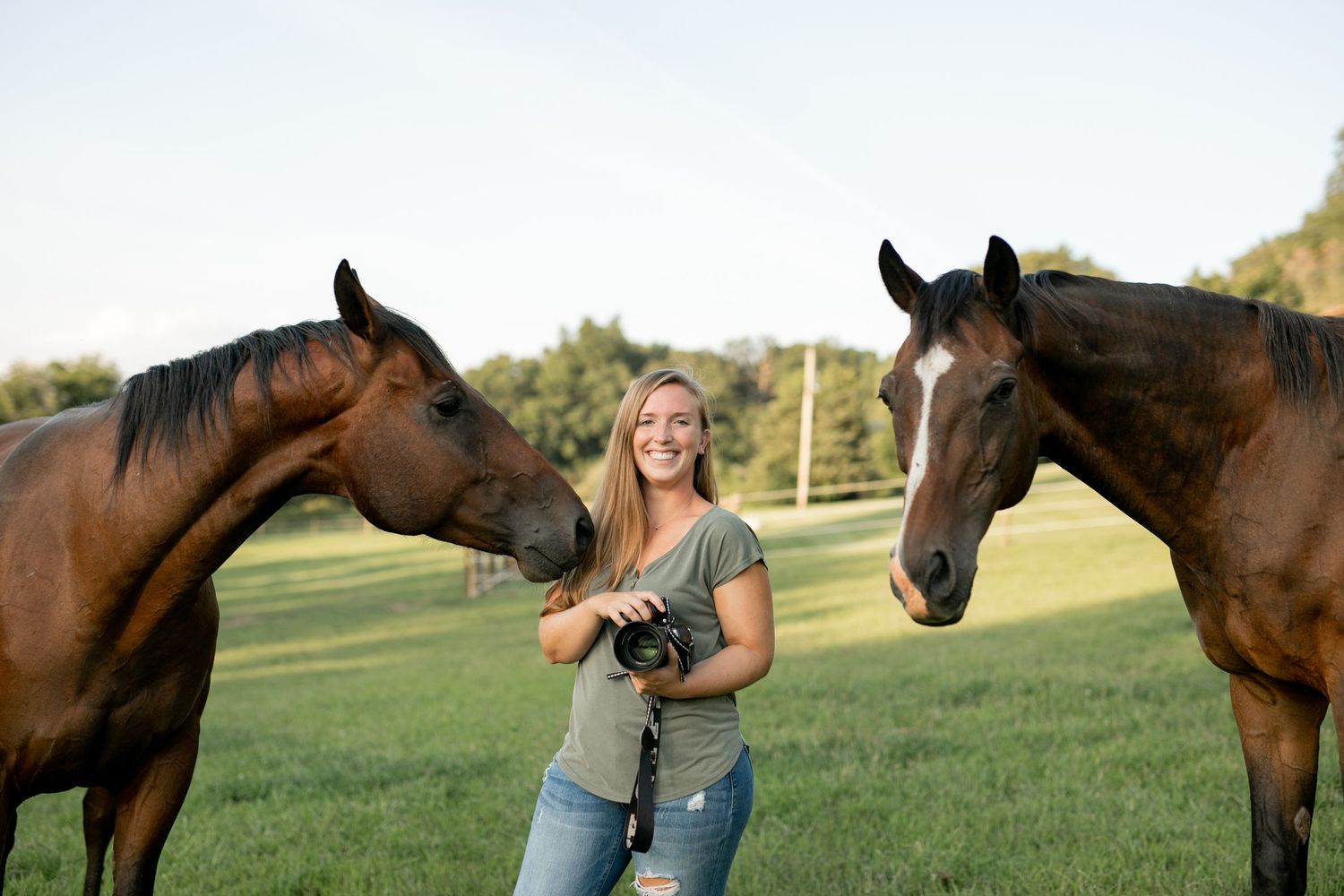 Two brown horses flank photographer with camera in golden evening light.