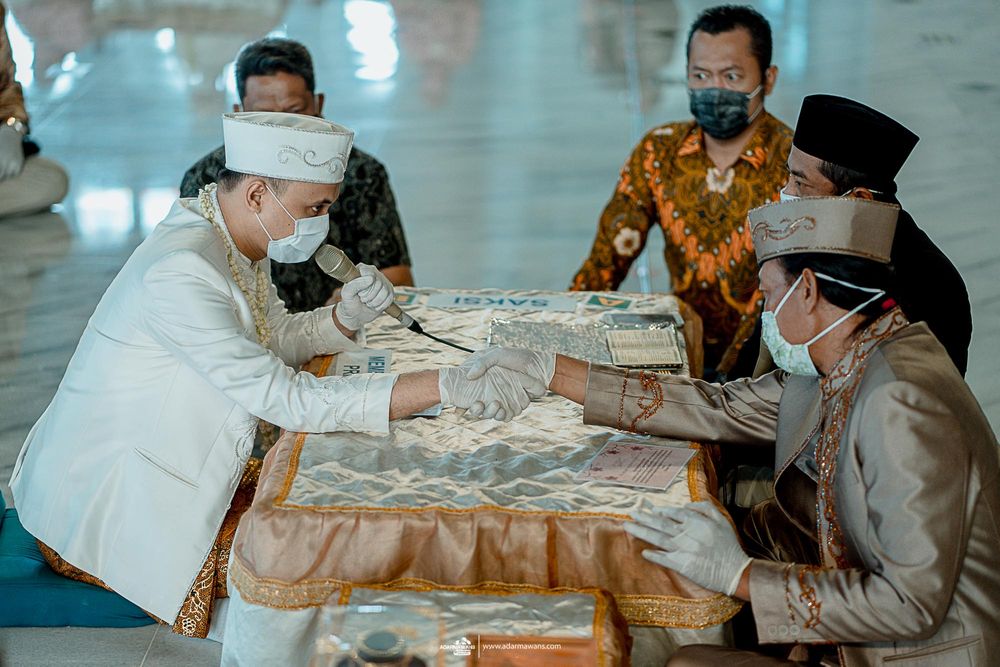 Participants in traditional dress sign documents at an ornate table during a ceremony.