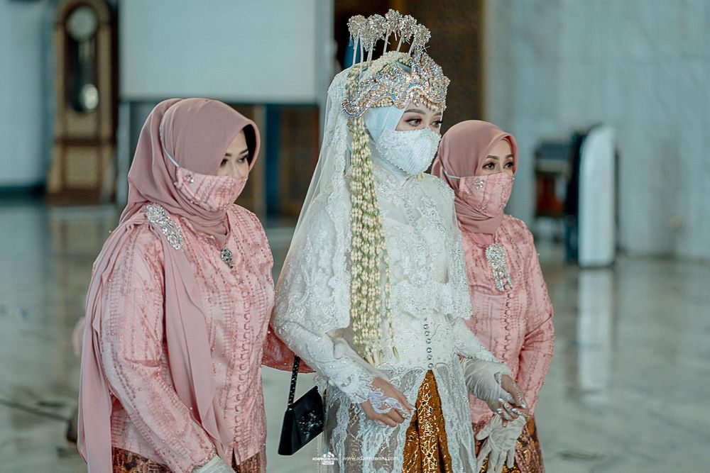 Three people in elegant traditional attire and face masks stand together during a ceremony.