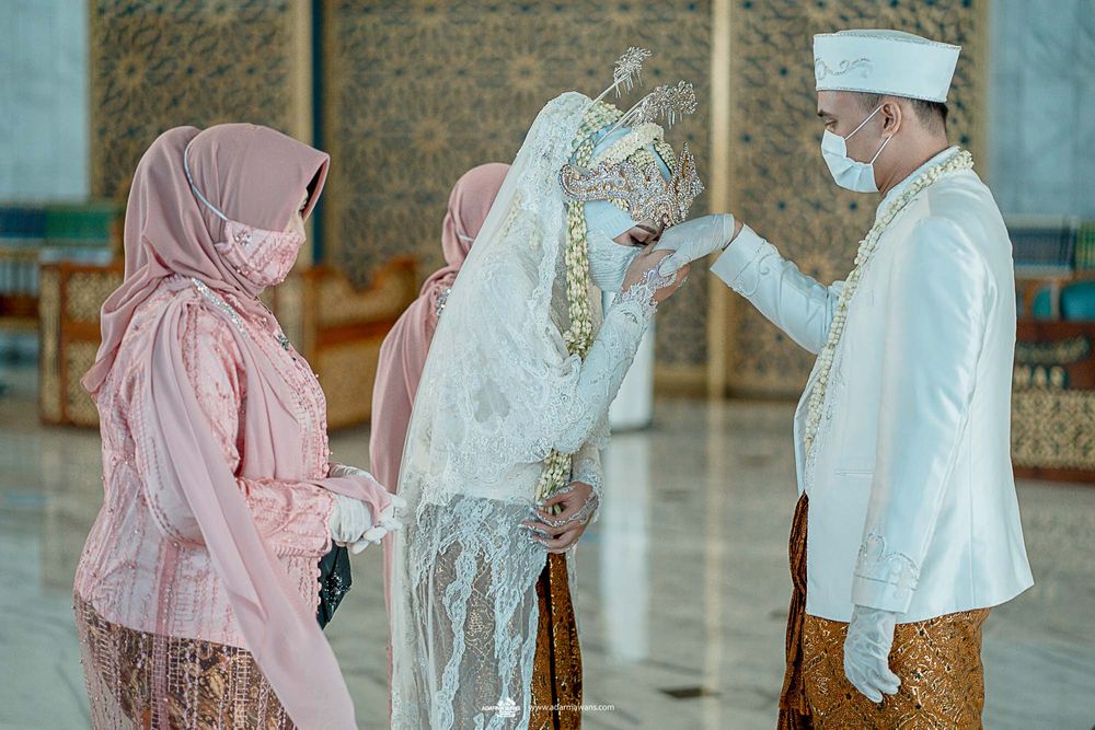 Attendees in traditional Indonesian dress and masks participate in a ceremonial interaction.
