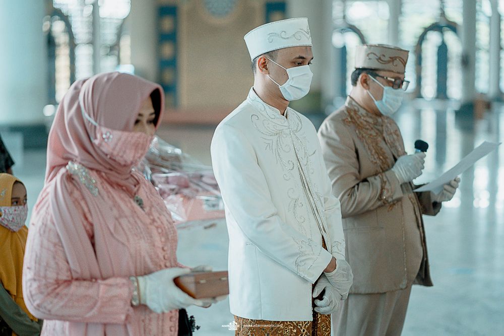 People in traditional Muslim attire wearing masks while participating in religious activities inside a mosque.