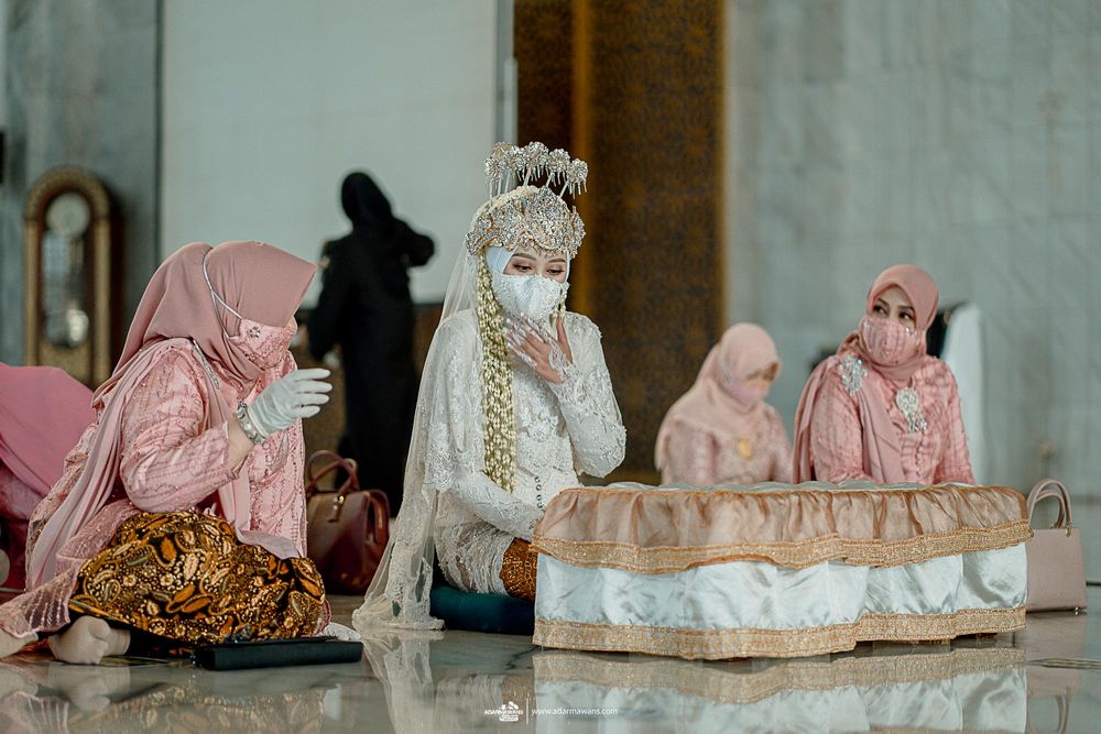 Women in hijabs and face masks sitting together during religious ceremony.