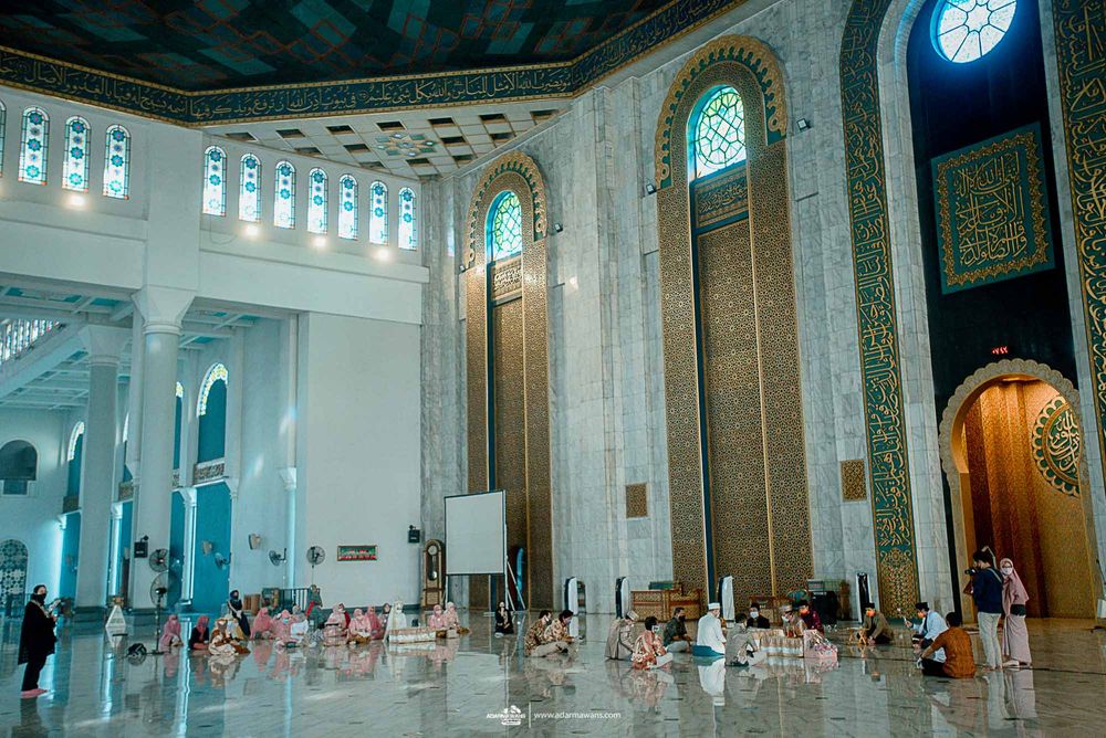 Interior of grand mosque with ornate architecture and stained glass windows illuminating marble floor.
