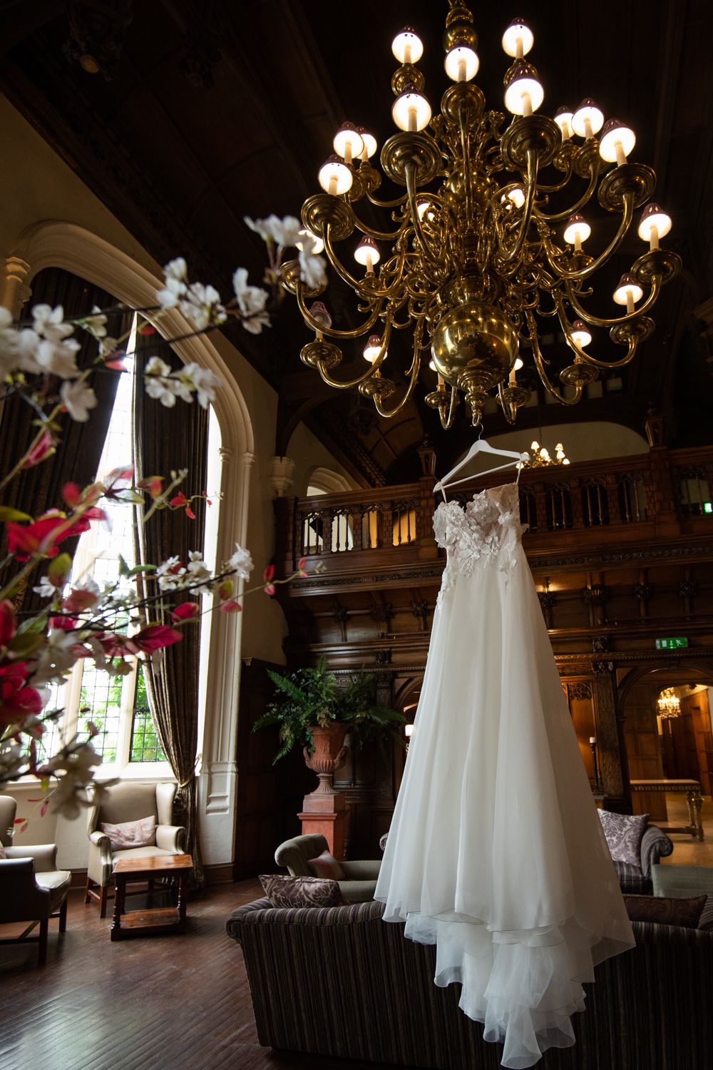 An elegant wedding dress hangs beneath a grand chandelier in a luxurious interior space.