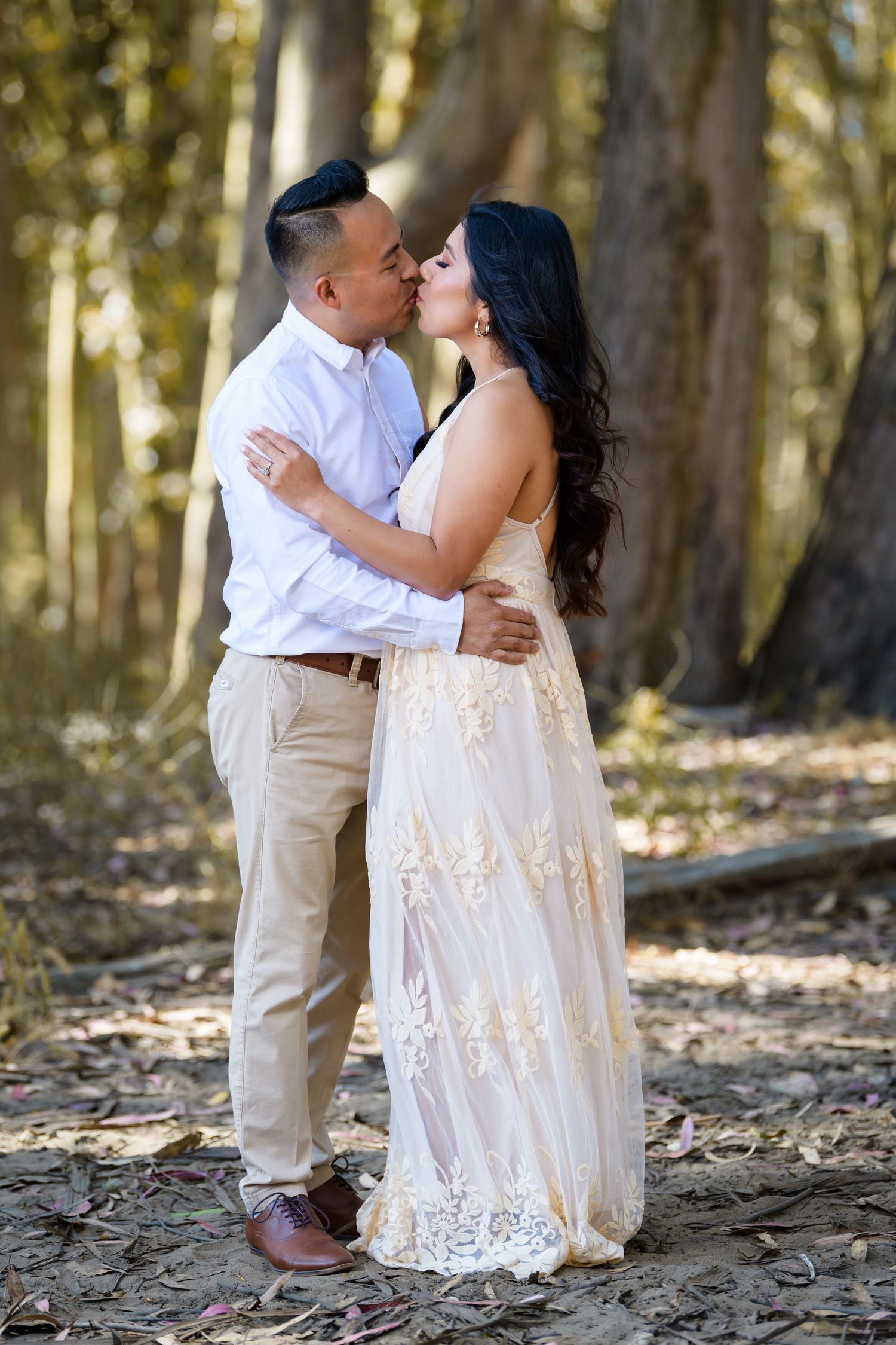 A romantic portrait of a couple sharing a tender moment in the woods, with golden sunlight filtering through the trees.