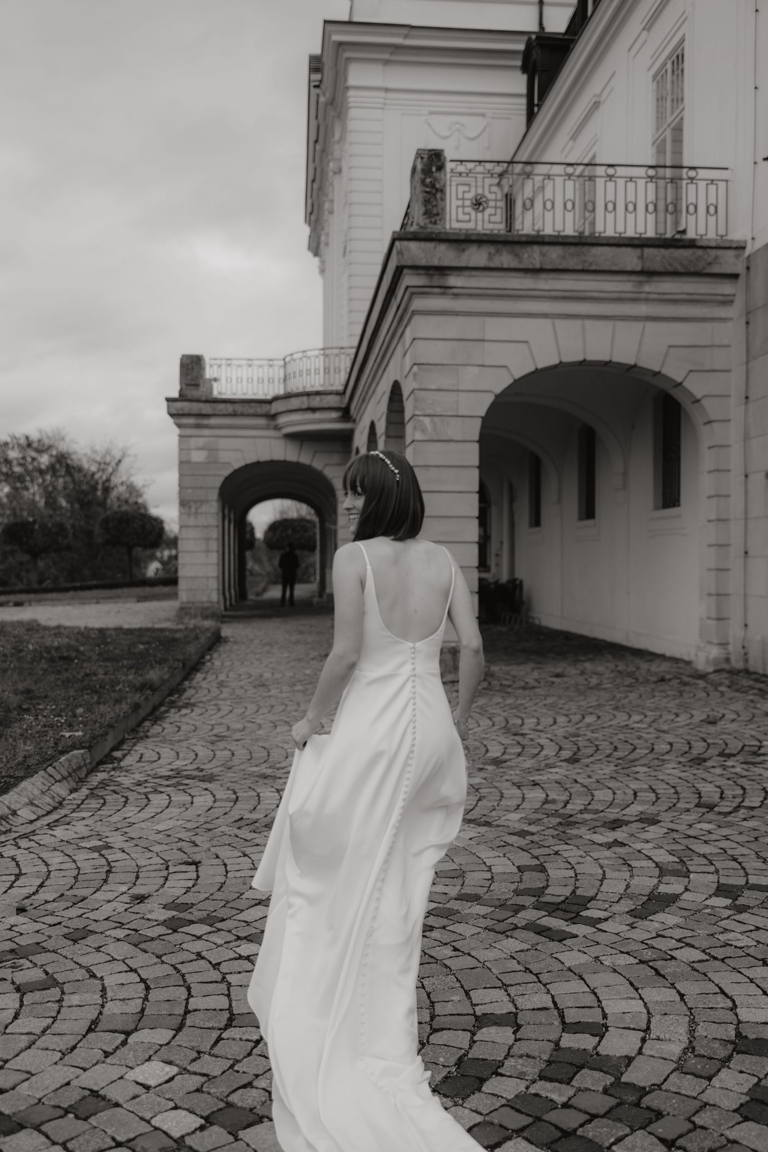 Bride in flowing dress walking on cobblestone courtyard in black and white.