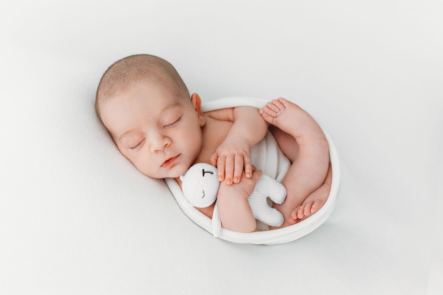 Newborn baby sleeping peacefully in white bowl during professional photo session.